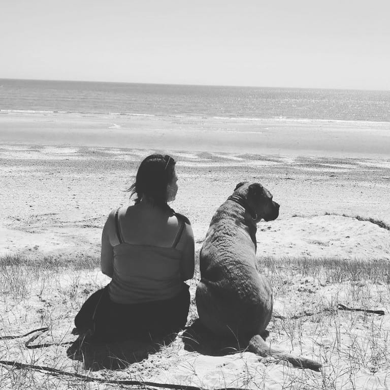 Amber, a dog walker, sitting at the beach with a big dog looking at the sea